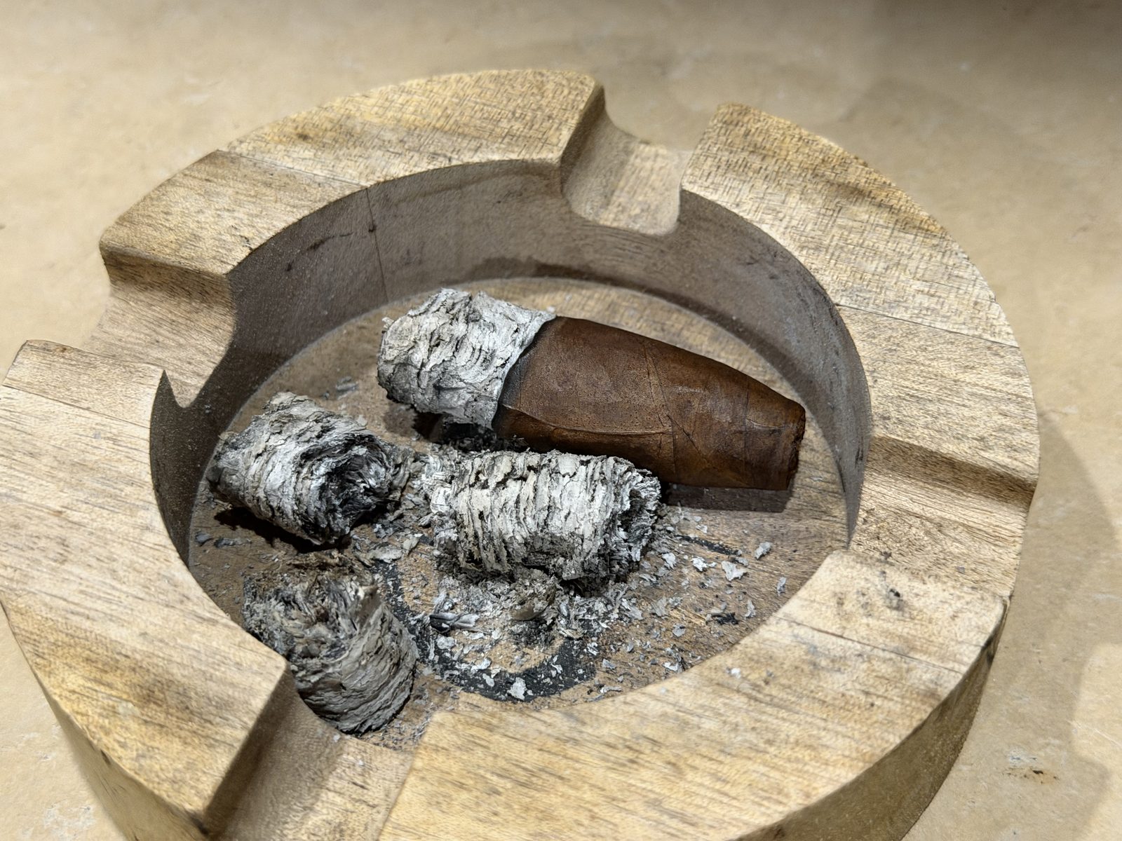 The end of the Aging Room Quattro Nicaragua Maestro laid down in a wooden ashtray next to several chunks of gray ash