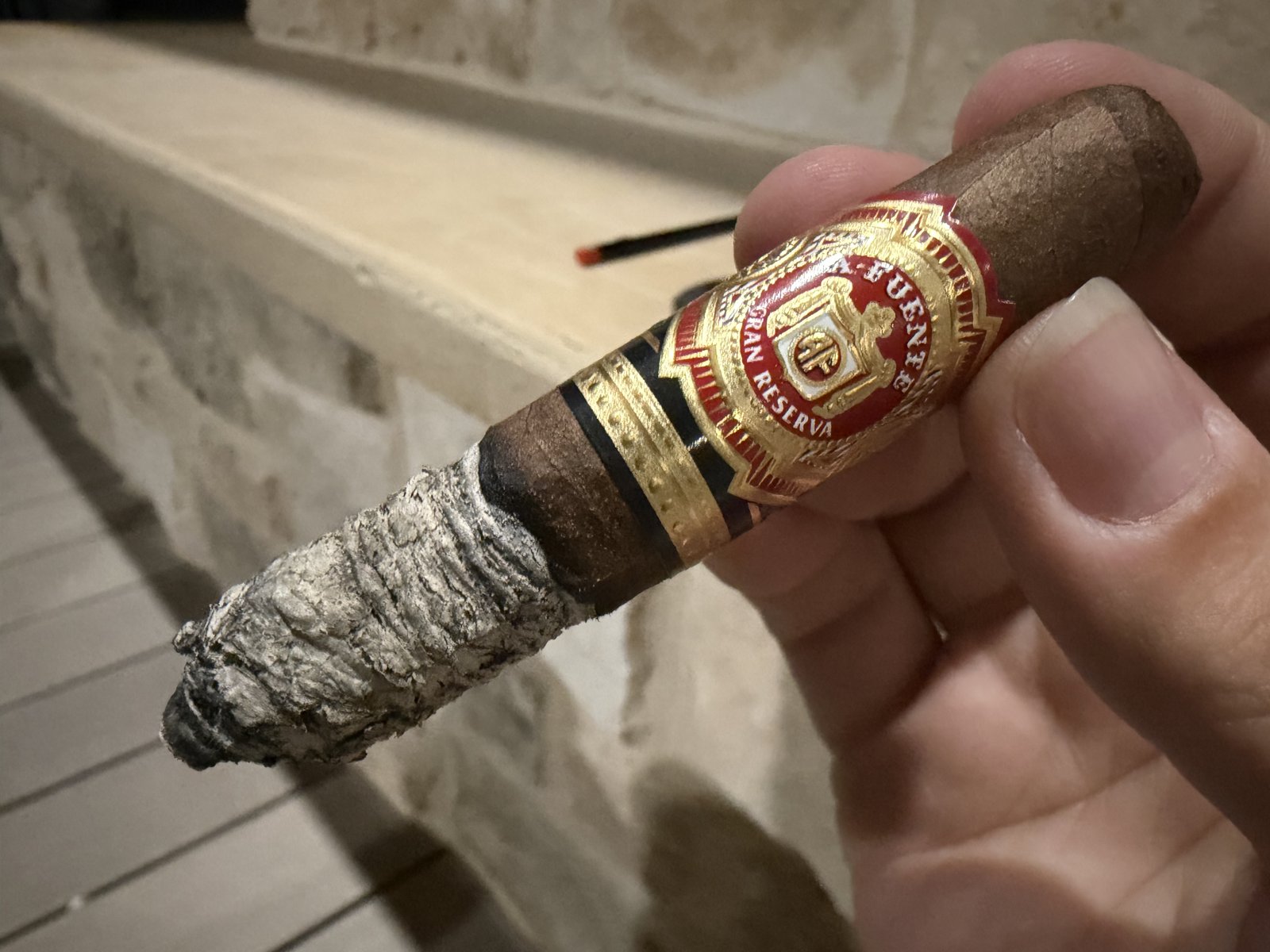 Arturo Fuente Hemingway Short Story burning with a flaky light gray ash stack, band still on, in front of a stone fireplace