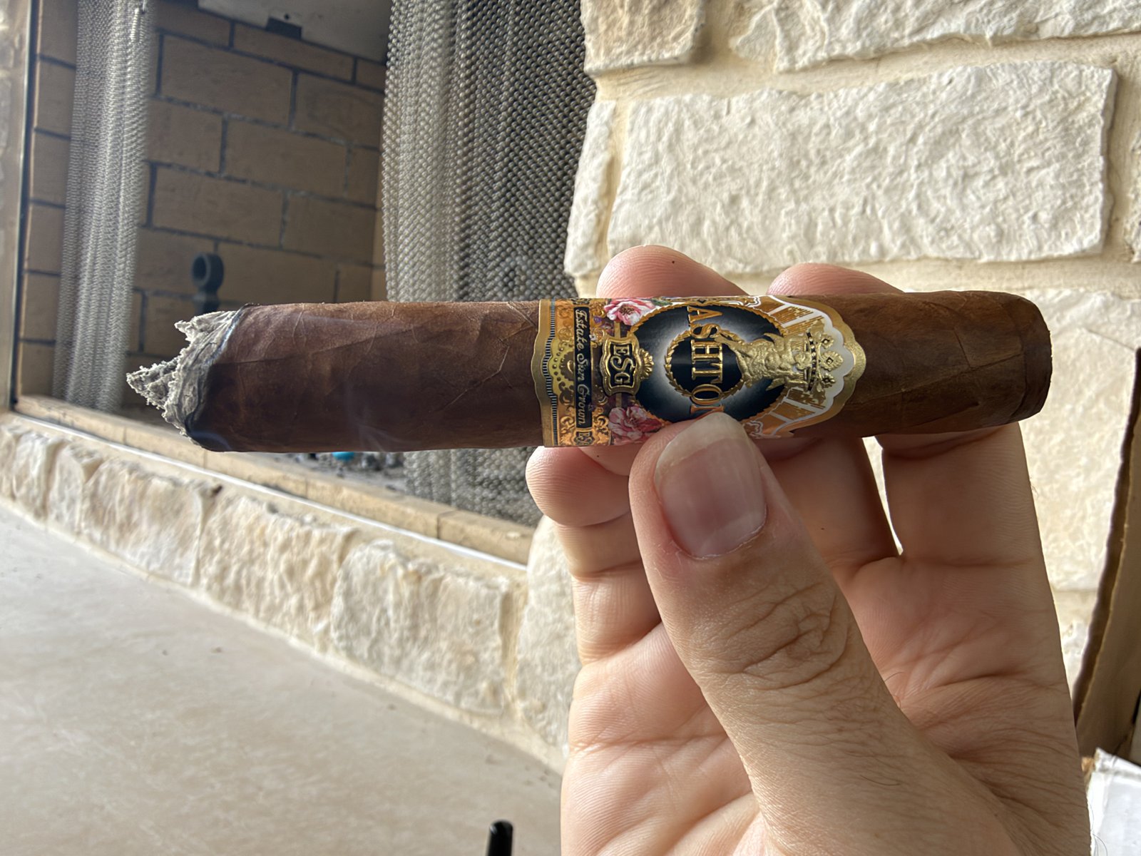 Ashton ESG 23 Year Salute Toro just after the first ash, showing the crooked burn line before the first touch-up, held in hand in front of a stone fireplace