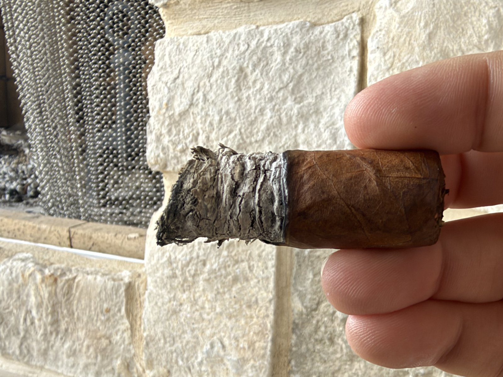 Nub of the Ashton ESG 23 Year Salute Toro held between two fingers at the end of the smoke, band removed, gray ash on the foot and a small unburnt fingernail of wrapper on the back side