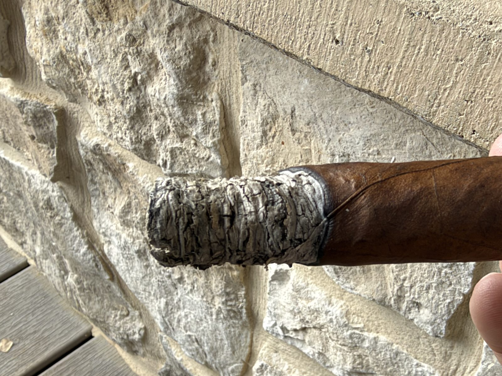 Ashton VSG Torpedo near the end of the first third, a layered gray ash and a burn line sitting much farther back on one side than the other, in front of a stone wall