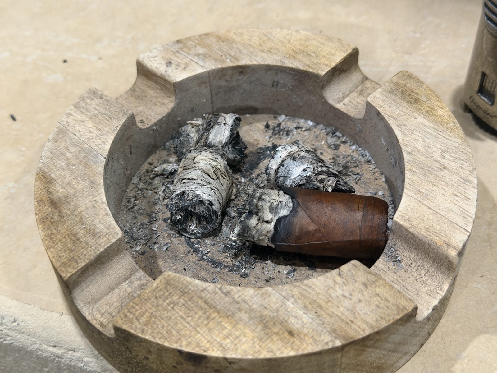 Wooden ashtray holding the Casa Magna Colorado Robusto with ash still attached to the foot, next to several pieces of gray and white ash