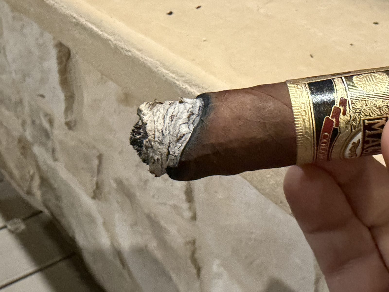 Casa Magna Colorado Robusto early in the second third with a badly crooked burn, one side of the ash and foot running well ahead of the other, band visible