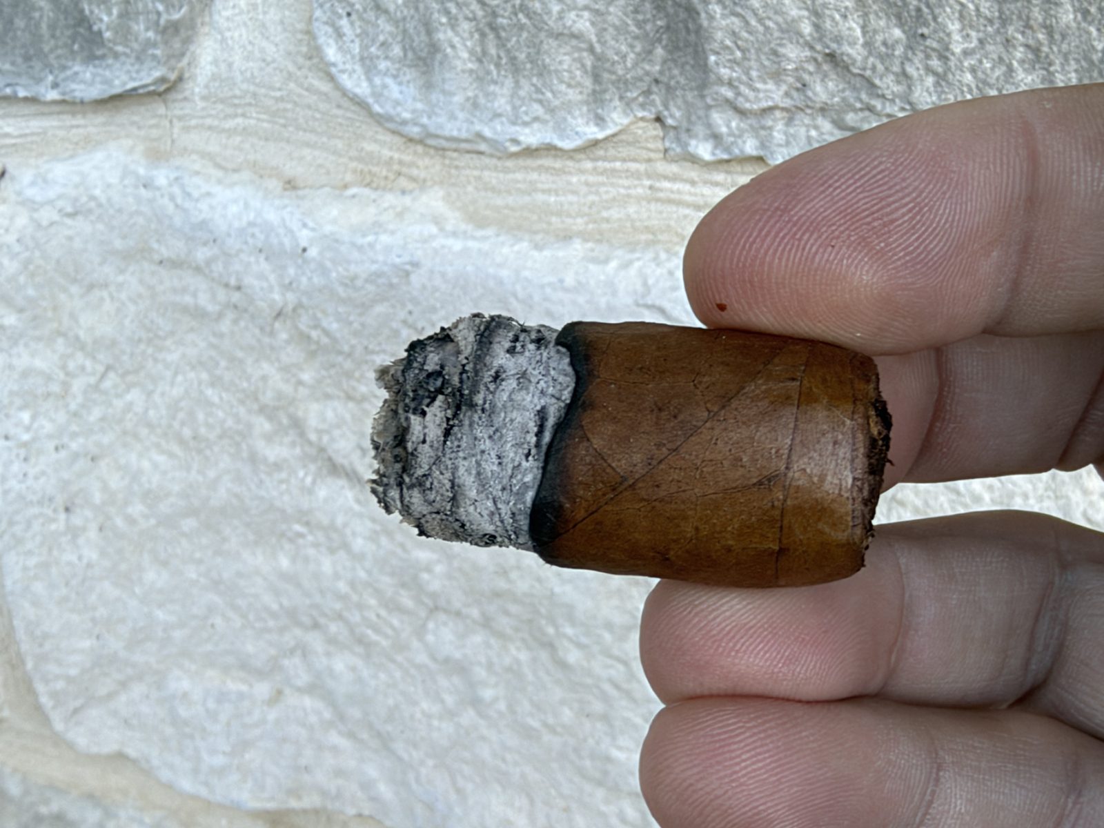 The nub of the Crowned Heads Mil Días Sublime held between two fingers, a short stub with a small ash on the end