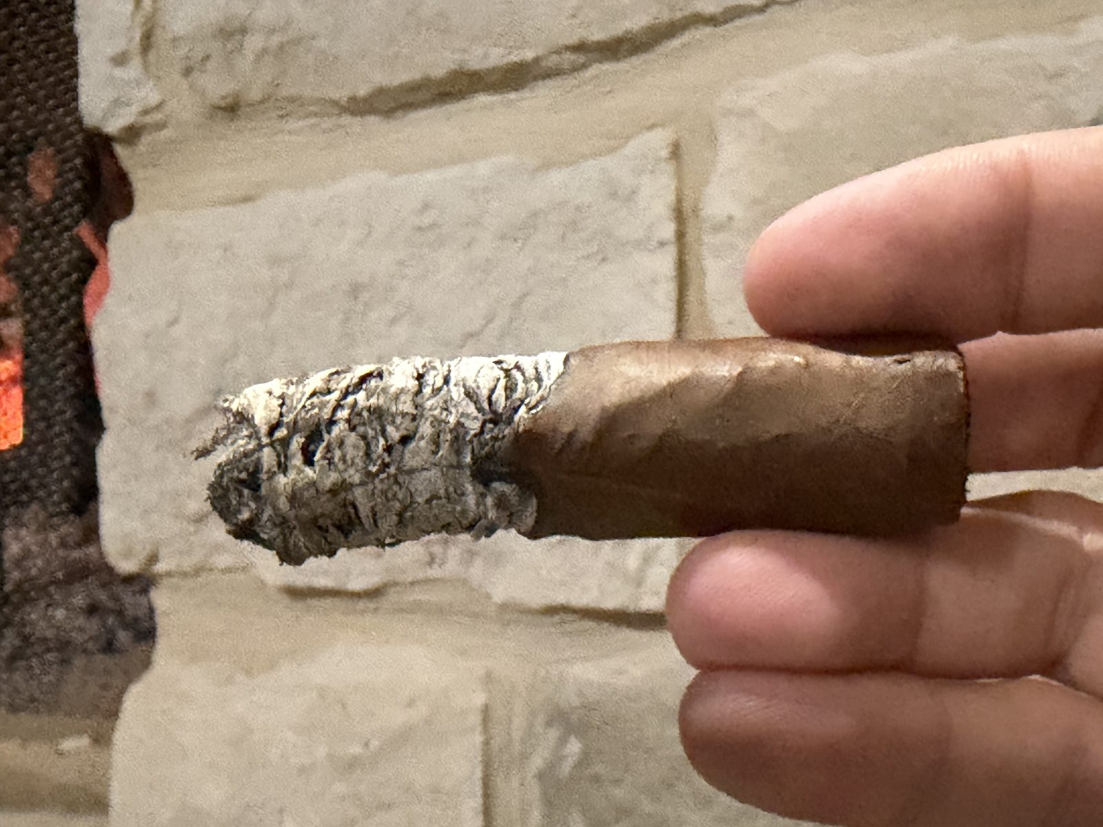 Diesel Uncaged Toro late in the final third with the band removed, a ragged gray ash and a slightly wavy burn line, held in fingers in front of a stone wall