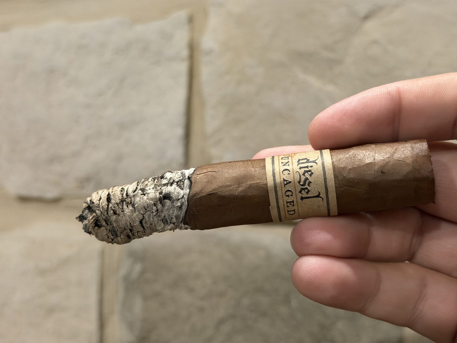Diesel Uncaged Toro at the end of the second third, a long, ragged gray ash and the band still on, held in fingers in front of a stone wall