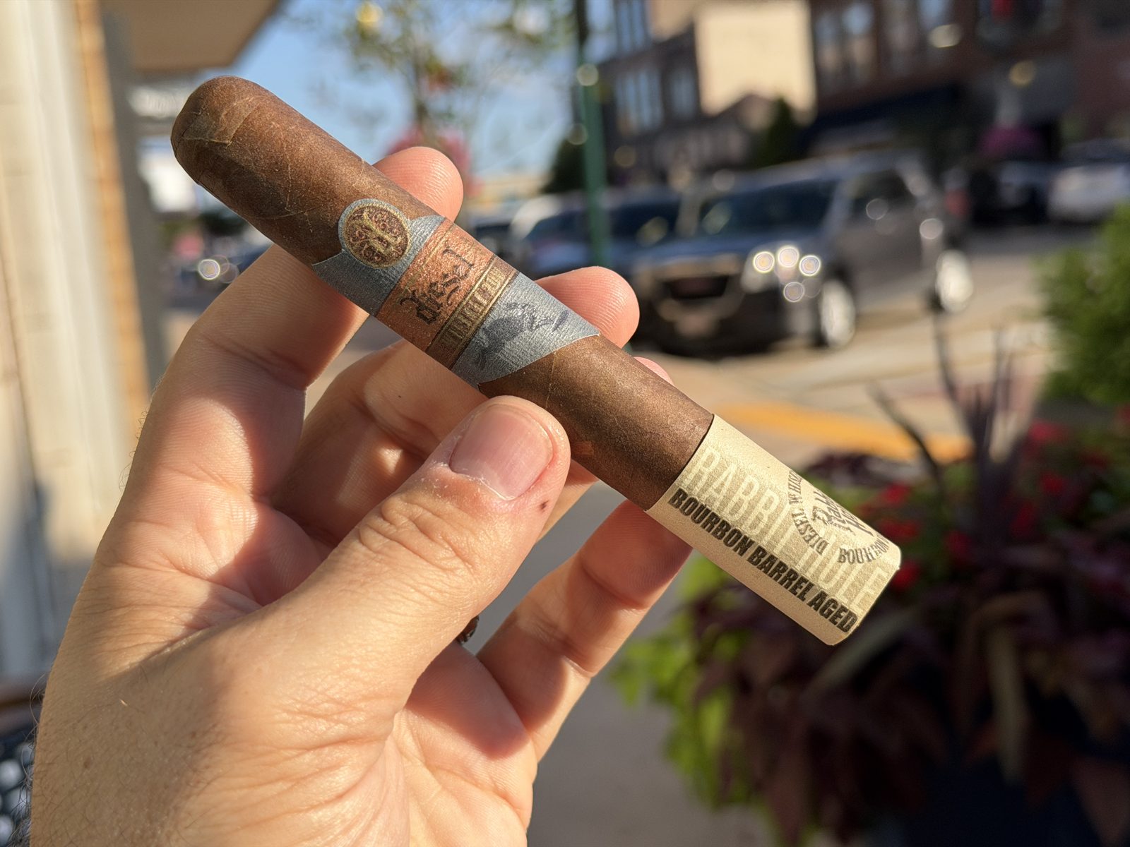 Diesel Whiskey Row Toro held in hand on a downtown sidewalk, medium-brown wrapper with the copper and slate Diesel band and a cream Rabbit Hole Bourbon Barrel Aged foot band