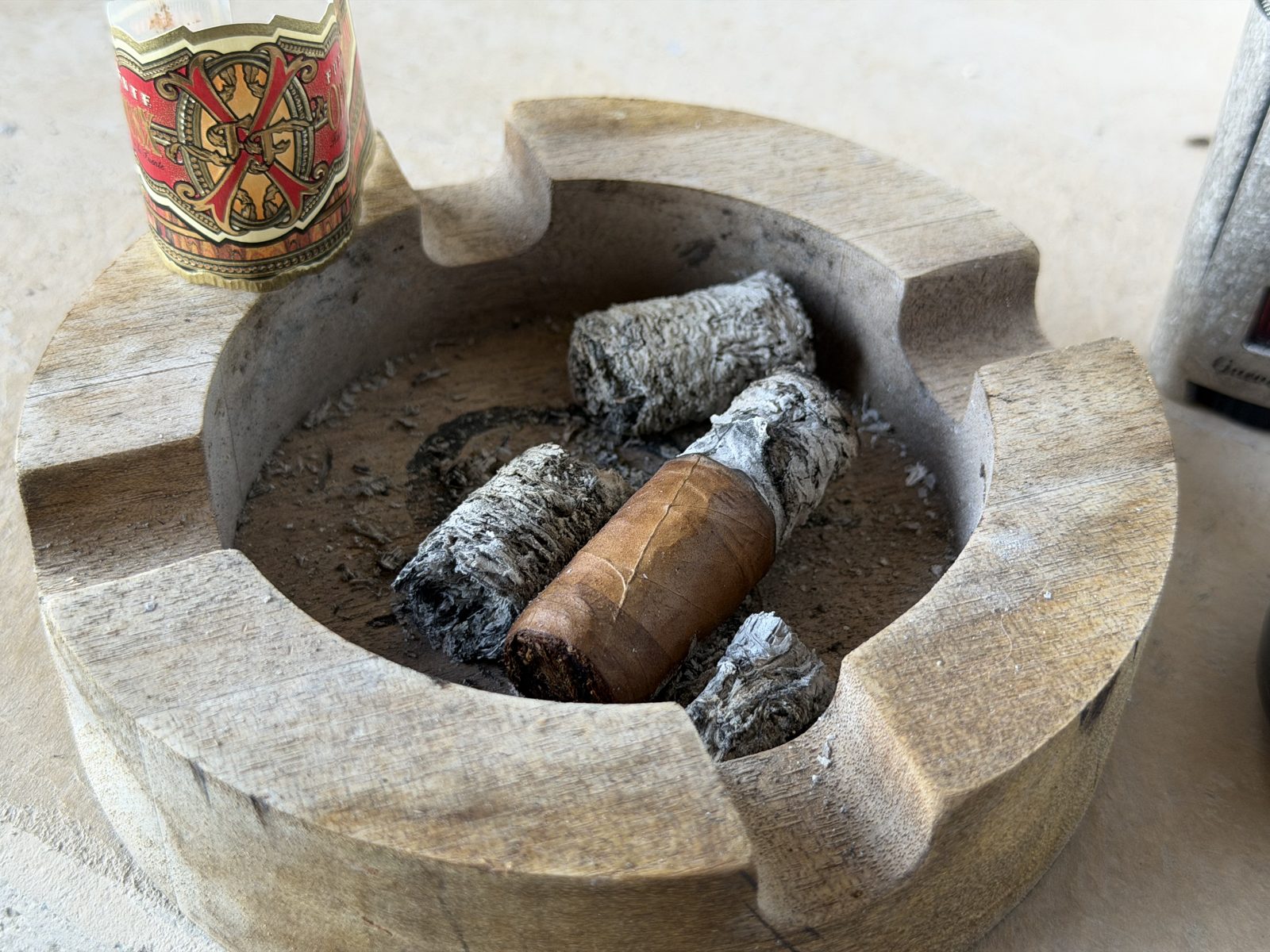 Wooden ashtray with the finished Fuente Fuente Opus X Perfecxion X nub, several piles of gray ash, and the removed Opus X band sitting on the rim