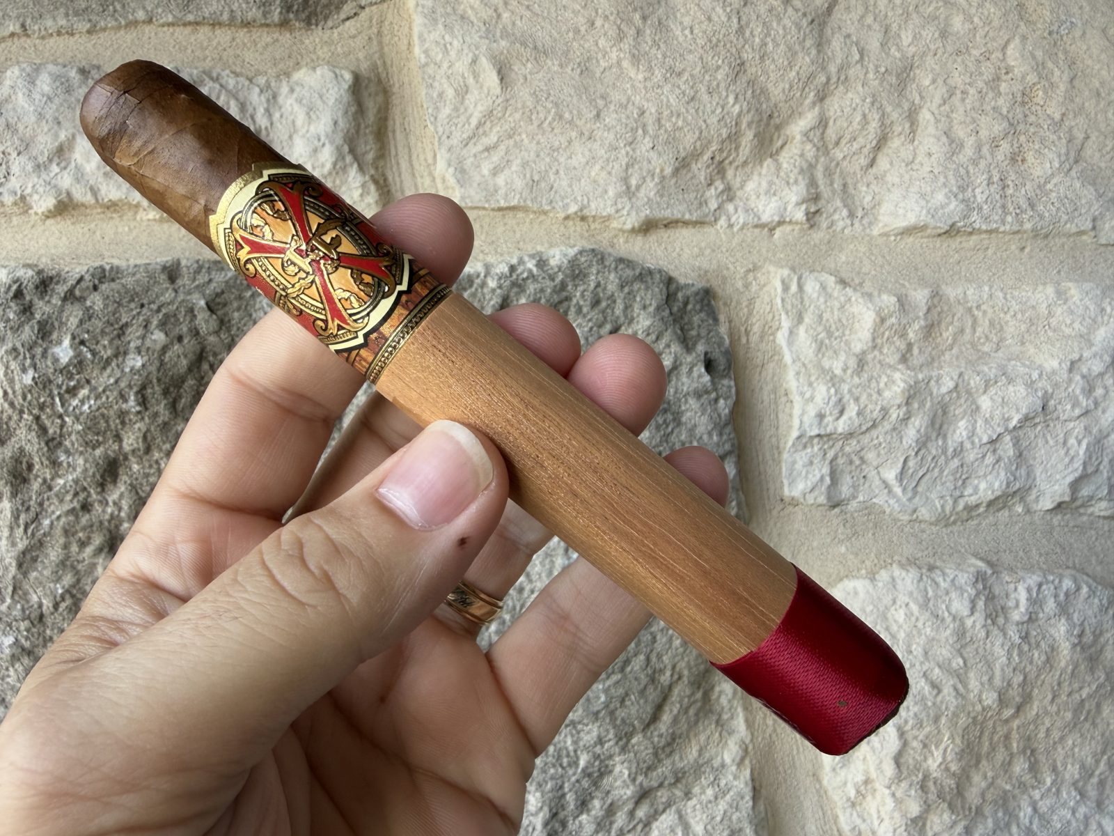Fuente Fuente Opus X Perfecxion X still in its full cedar sleeve with a red ribbon over the foot, held in hand against a stone wall