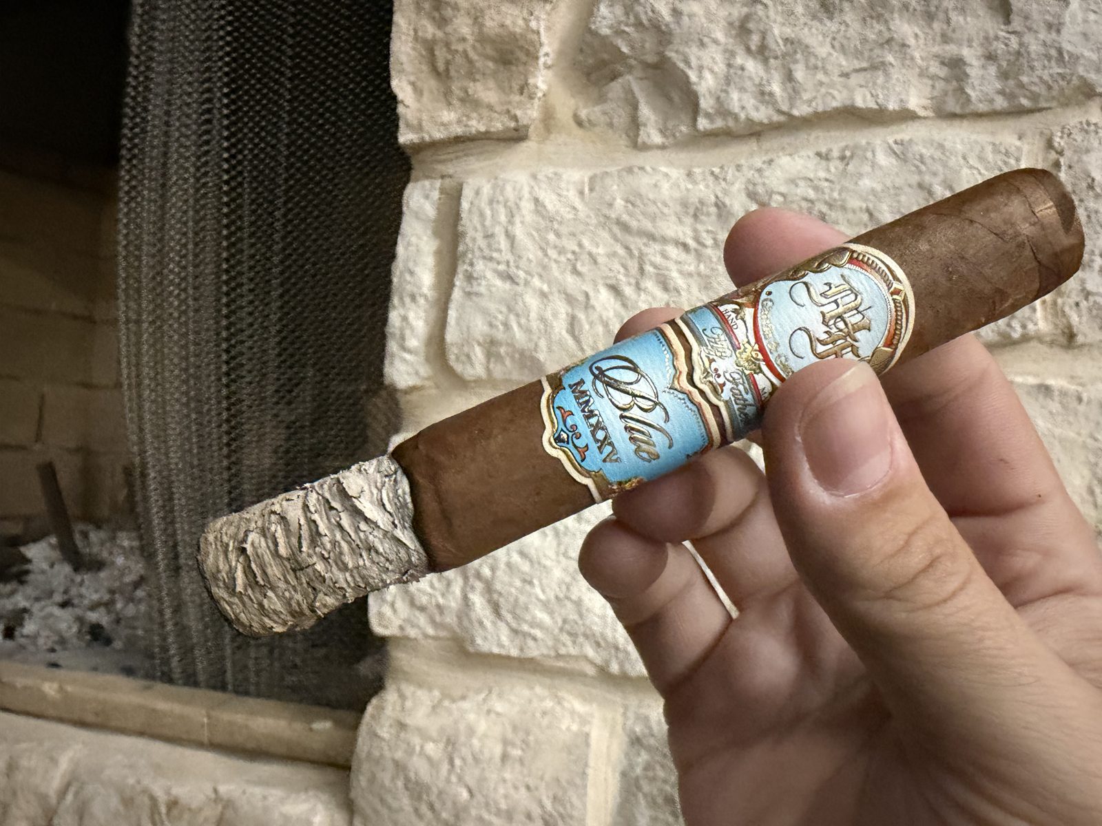 My Father Blue Toro burning in the first third with a tight gray ash, both bands still on, in front of a stone fireplace