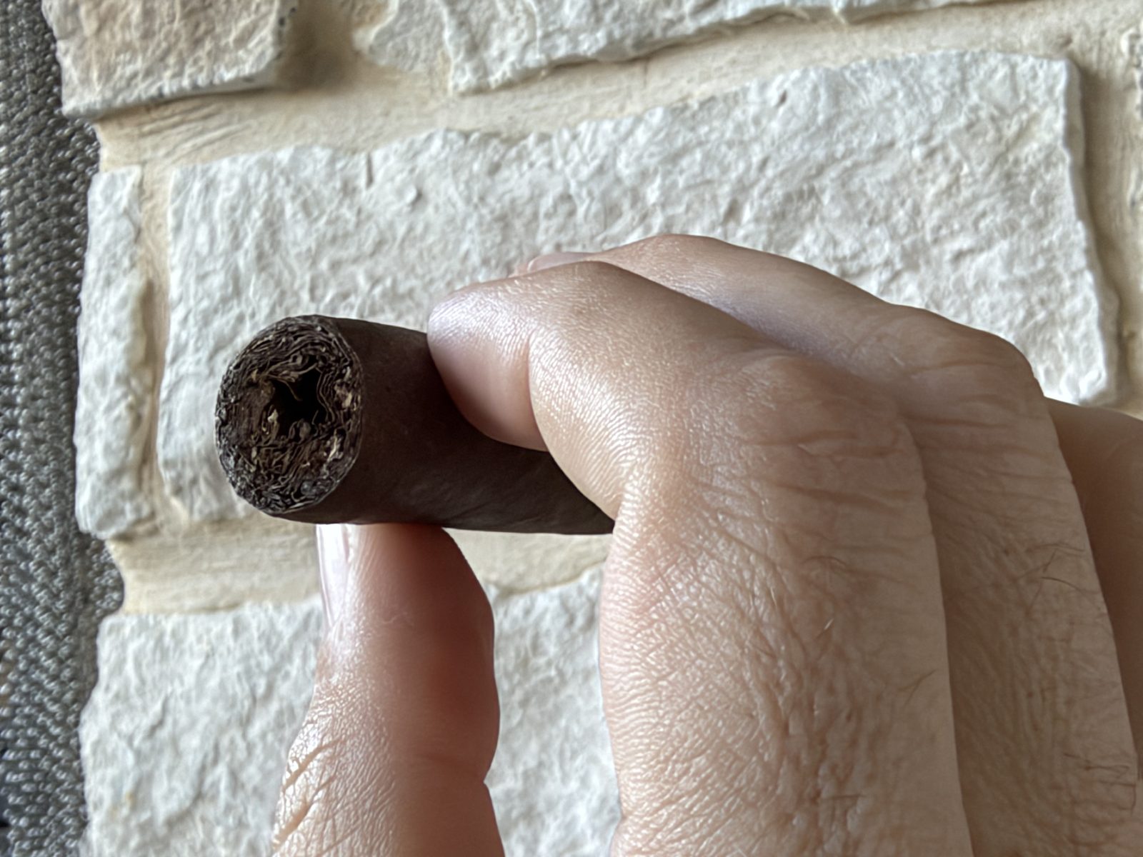 Close-up of the cut head of the Oliva Serie V Maduro Toro showing the loosened filler where the draw tool went in, held in fingertips against a stone wall