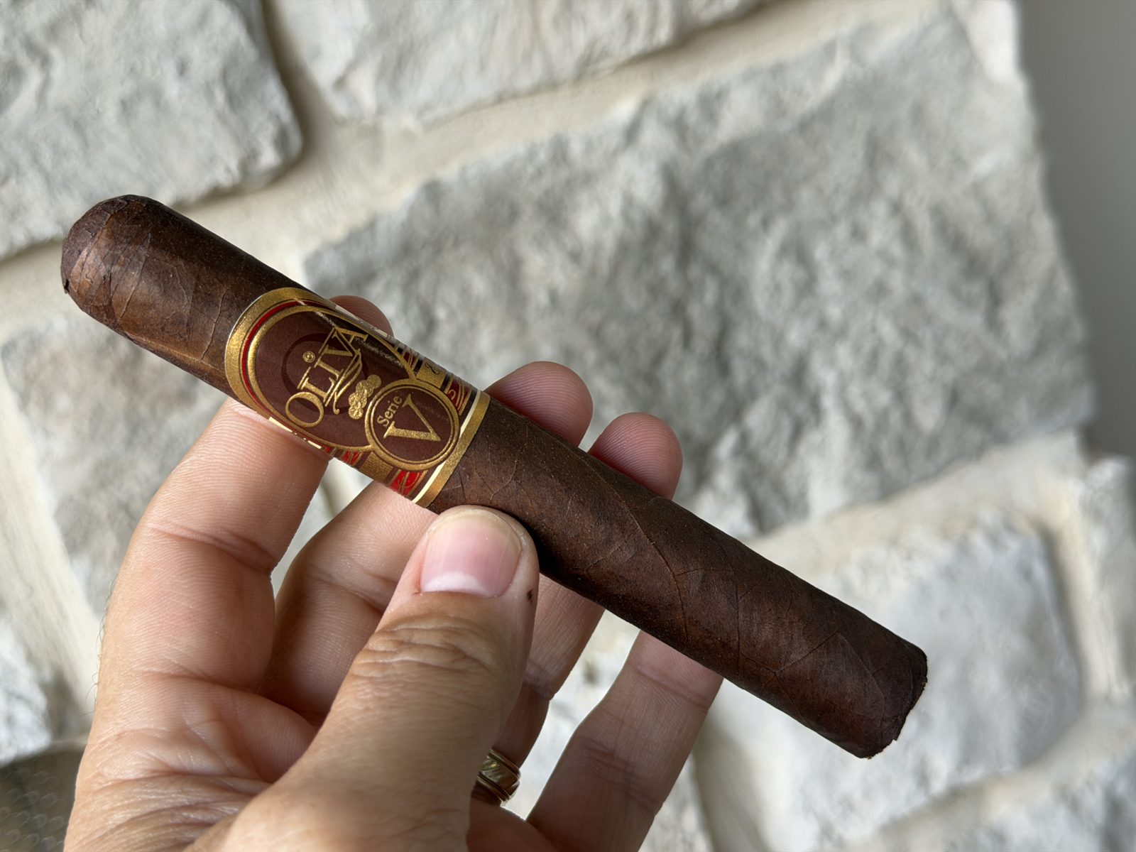 Oliva Serie V Toro held in hand against a white stone wall, chocolate brown wrapper, gold and red Serie V band