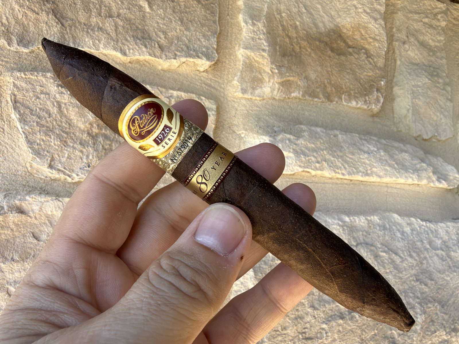 Padrón 1926 Serie 80 Years Maduro perfecto held in hand before lighting, dark toothy maduro wrapper with the 1926 Serie band and the 80 Years band