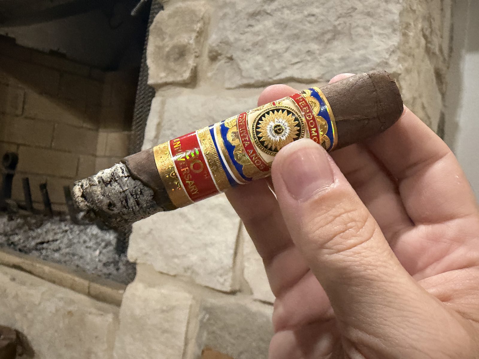 Perdomo 30th Anniversary Maduro Epicure burned down to the band, with the ash and burn line running crooked, one side right at the band and the other side well short of it, held in hand with a fireplace behind