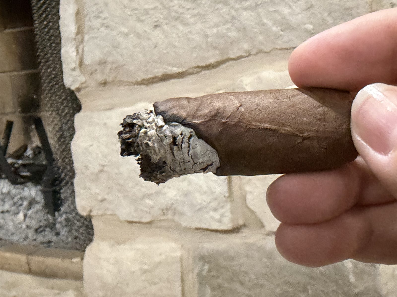 Perdomo 30th Anniversary Maduro Epicure in the final third with the band off, a thin ragged ash and the burn line badly uneven from one side to the other, held in fingers in front of a fireplace