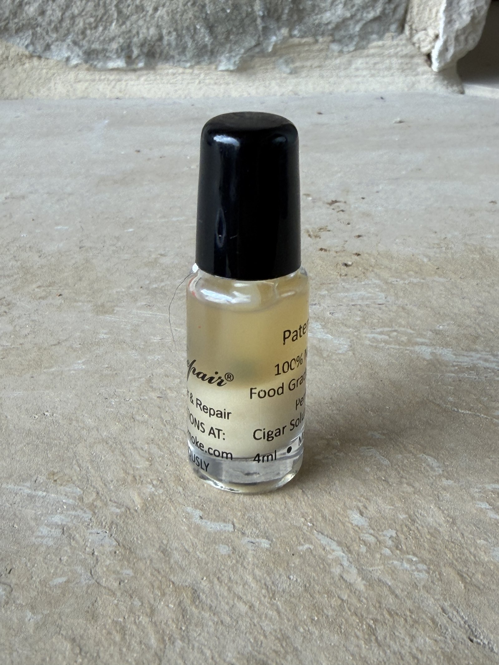 PerfecRepair cigar glue, small 4ml glass bottle with black brush cap, on a stone hearth