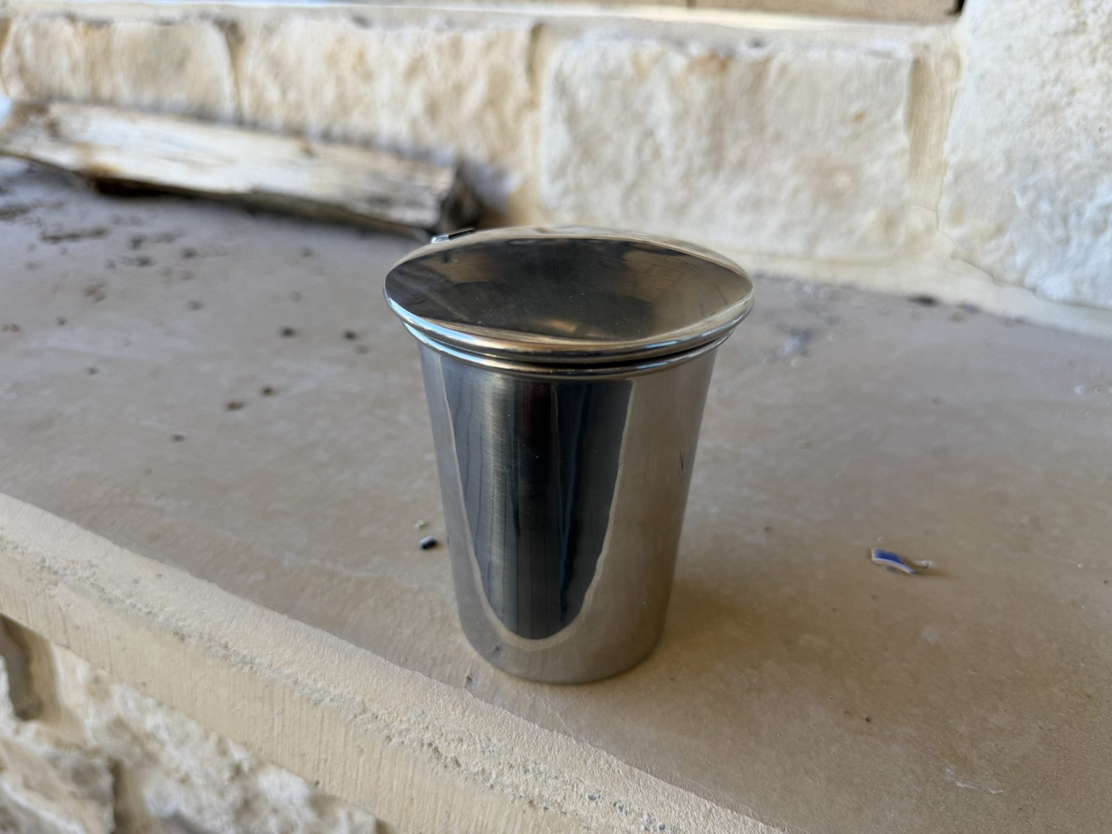 Stinky Cigar Car Ashtray closed, polished stainless steel cup with the lid shut, sitting on a stone ledge