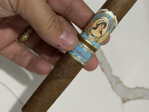 La Aroma de Cuba Mi Amor Magnifico held in hand, box-pressed medium-brown wrapper with the light-blue La Aroma de Cuba señorita primary band and a light-blue and gold Mi Amor secondary band