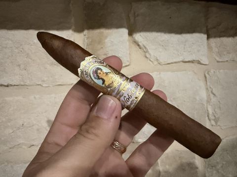 Unlit La Aroma de Cuba Noblesse Viceroy held in hand against a stone wall, a chocolate brown San Andrés wrapper on a torpedo with the light purple and gold señorita band