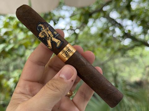 Room101 Johnny Tobacconaut JT10 toro held in hand before lighting, dark wrapper with the gold astronaut band and JT10 foot band