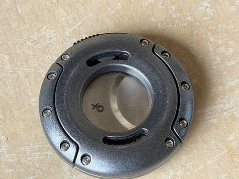 Xikar XO cutter in gunmetal, closed, round body with exposed screws on a stone surface