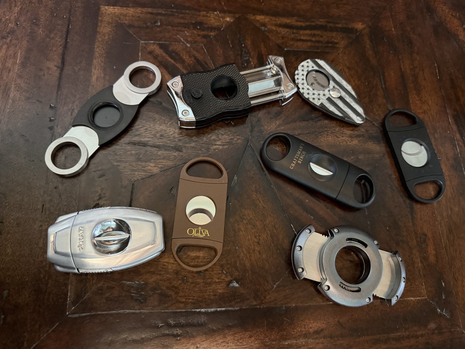 Seven cigar cutters laid out on a dark wood table